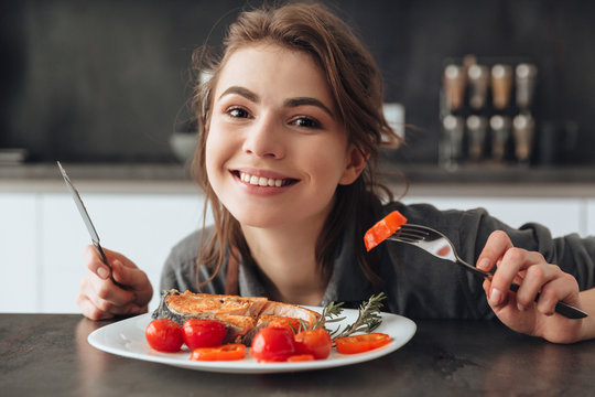 Happy young lady eating fish and tomatoes.