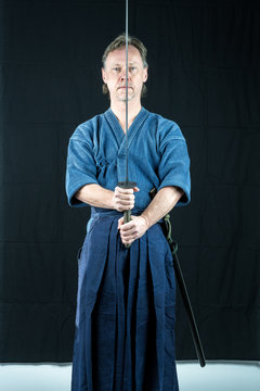 Adult caucasian male training Iaido holding a Japanese sword with focused look. Studio shot with black background.