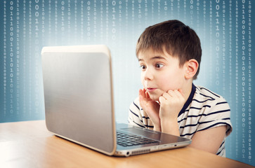 surprised seven years old child sitting with a laptop at table
