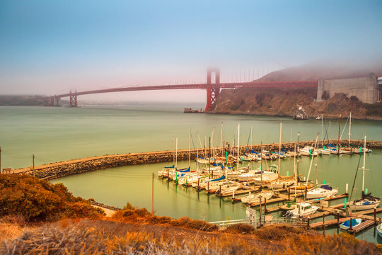 Aerial view of Golden Gate Bridge with typical fog and Presidio Yacht Club in Horseshoe Bay, Sausalito, California, United States. Symbol and landmark of San Francisco. Travel and holidays concept.