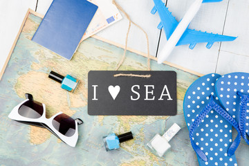 blackboard with text "I love SEA", plane, map, passport, money, flops and other accessories