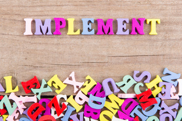 Text "Implement" of colored wooden letters on a wooden background
