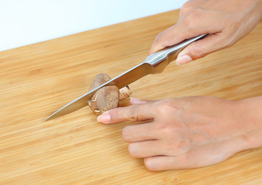 Sharp knife on woman hands cut Shiitake mushroom on wooden block
