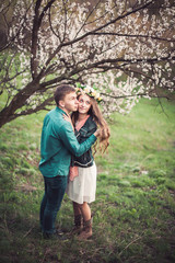 Young couple in love having a date under pink cherry blossom trees in sunset time. Love and tenderness in spring season