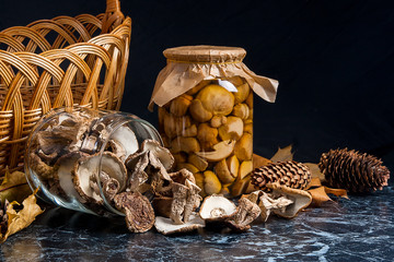 Two glass jars with wild mushrooms on black marble background.