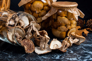 Two glass jars with wild mushrooms on black marble background.