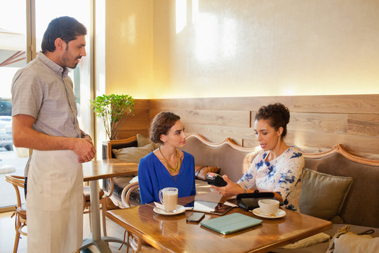 Expat woman paying using credit card reader at restaurant.