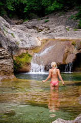 Beautiful nature, girl in bikini swimsuit enjoying bathing near natural waterfall in lagoon at summer sunny day