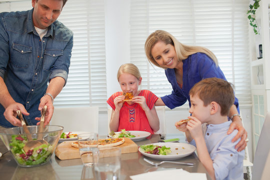 Parent with children eating pizza at home.