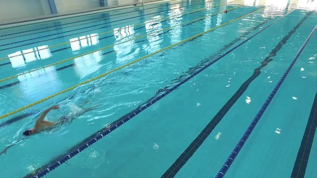 Flight over male swimmer swims in a pool HD aerial video. Front crawl freestyle training. Professional athlete on water lane