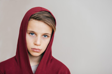 Portrait of a young attractive boy in red hoodie on a light background