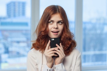 a woman near the window with a surprised look holds the phone in her hand