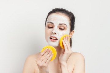 woman wipes cream from face with yellow sponges
