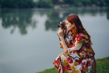 the woman is sitting near the river and is holding a camera