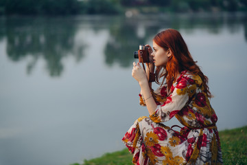 the woman is sitting near the river and is holding a camera