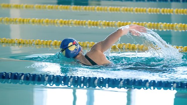 Female swimmer swims in pool HD slow-motion video. Front crawl freestyle training of professional woman athlete. Water splashing. Side view