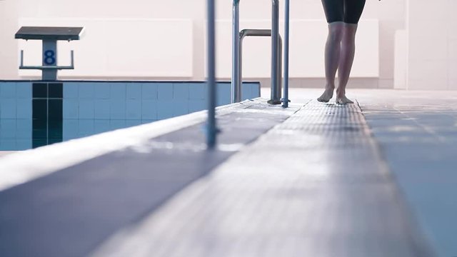 Female swimmer barefoot leg foots walking on swimming pool rubber flooring HD slow-motion video. View of lower body and foot steps of athlete