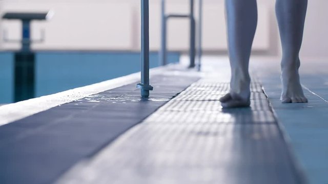 Female swimmer barefoot leg foots walking on swimming pool rubber flooring HD slow-motion video. View of ankle and foot steps of athlete