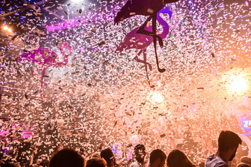Two small inflatable pink flamingos form a heart with their necks. In the background there is the head of a big flamingo © mattia_b