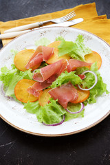 Salad with jamon and persimmon on the plate on dark background