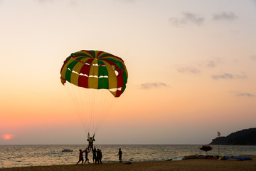 People enjoy parasailing at beach during sunset time