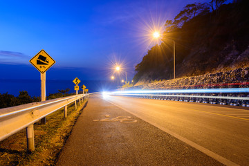 The road with car lights on the hill near the coast at night