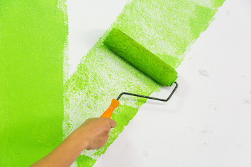 Man hand with roller brush painting green color on wall