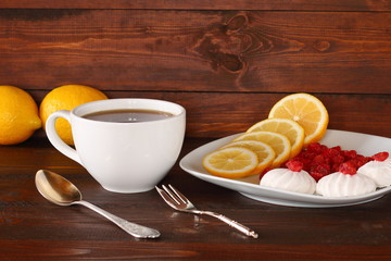 Кружка с чаем и тарелка с лимоном, сушеной вишней и зефиром на темном деревянном фоне.