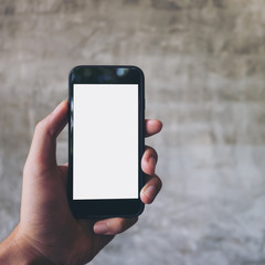Mockup image of hand holding black mobile phone with blank white screen on concrete polishing wall background 