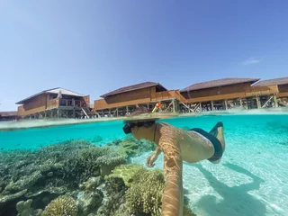 Fototapeten Young man snorkeling underwater on a colorful coral reef of Maldives island. © tirachard