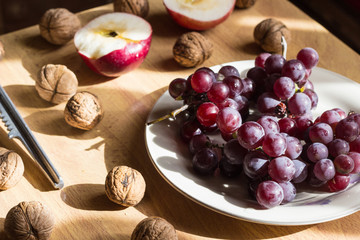 Apple, nuts and grape on wooden table in bright light