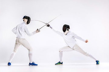 The two men wearing fencing suit practicing with sword against gray