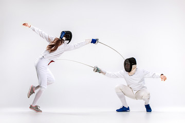 The woman and man wearing fencing suit practicing with sword against gray