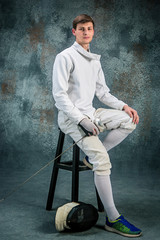 The man wearing fencing suit with sword against gray