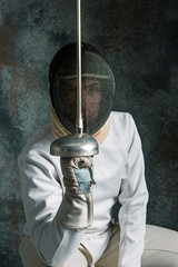 The man wearing fencing suit with sword against gray