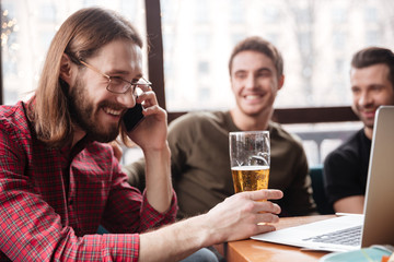 Men friends sitting in cafe drinking beer. Talking by phone.