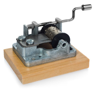 The mechanism of silver music box with a handle on a wooden board. Musical toy in a side view, at an angle on a white background with light reflection.