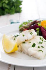 Fried cod fillet and salad in plate on white wooden background
