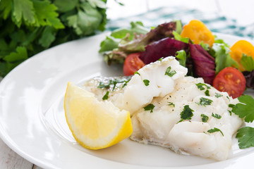 Fried cod fillet and salad in plate on white wooden background
