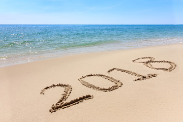 Year 2018 written at the sand beach with sea wave water