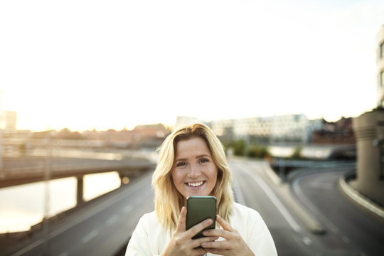Portrait of happy woman with mobile phone against sky