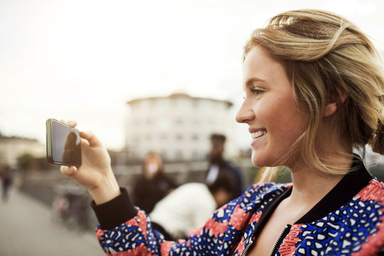 Side view of happy woman photographing from a smart phone