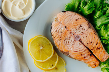 Baked salmon with lemon on white plate top view