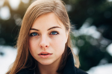 Closeup portrait beautiful blue eyes girl in black coat walking in winter park