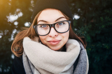 Portrait of a beautiful girl with blue eyes in black glasses in a black hat and coat with scarf in...