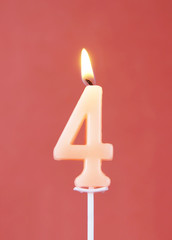 Burning wax candle as number four on red background