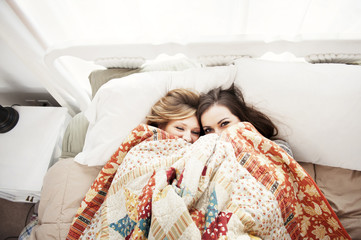 Two friends hiding under covers in bed