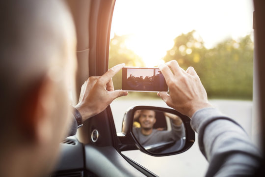 Rear view of man photographing from mobile phone with reflection in side-view mirror