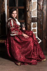 Medieval style portrait of attractive woman in red dress with wine glass in her hands
