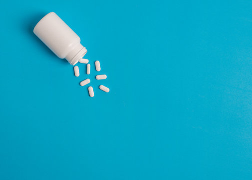 White Pills And Pill Bottle On Blue Sky Background.